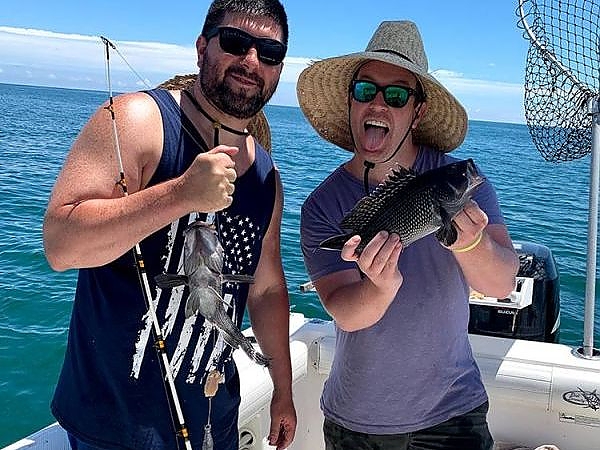 Two men on boat under roof pose with their fish